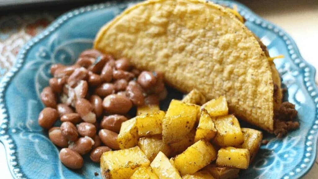 A taco, beans, and taco potatoes on a blue plate.