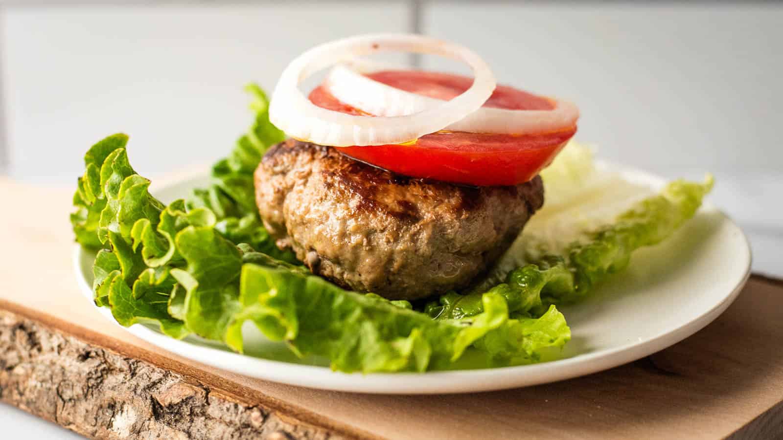 A turkey burger lettuce wrap with tomato and onion on a white plate.