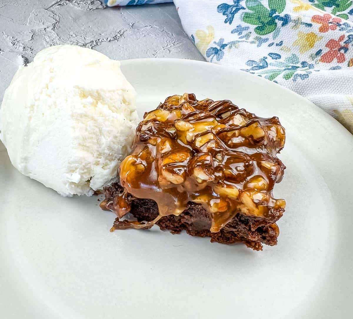A piece of Turtle Brownie with ice cream on a plate.
