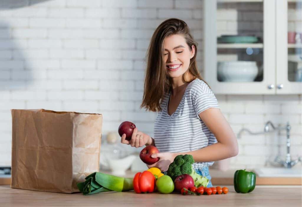 A young woman is standing next to a paper bag full of vegetarian vegetables.