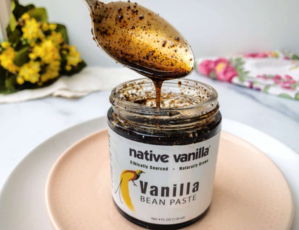 A spoon is being poured into a jar of vanilla bean paste.