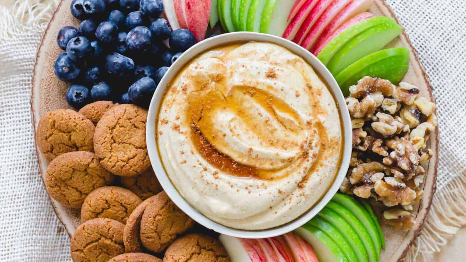 Whipped pumpkin ricotta dip on a wooden tray with cookies, walnuts and fruit.