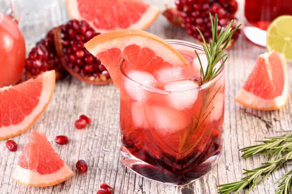 A glass of pomegranate juice mocktail with rosemary sprigs.