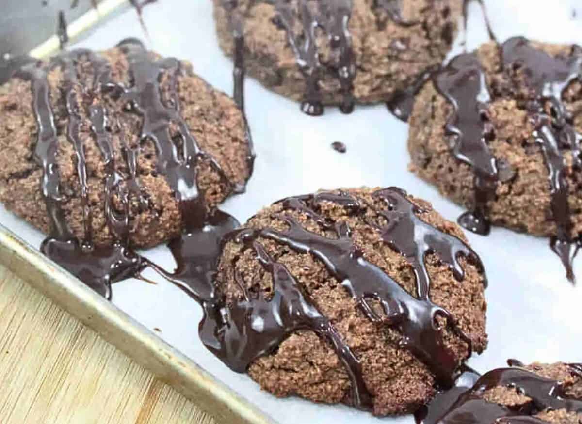 Chocolate almond flour cookies drizzled with chocolate on a piece of parchment paper.