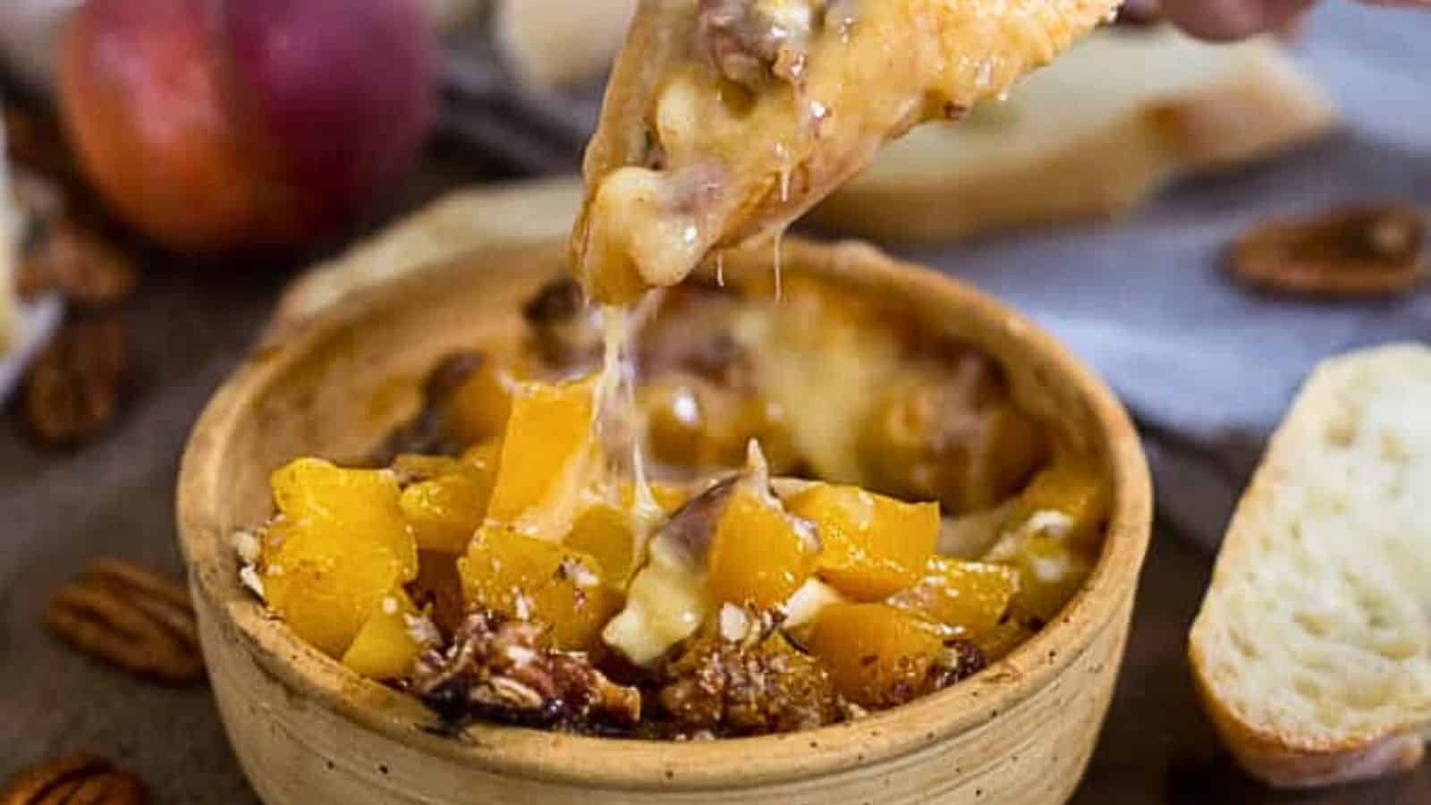 A person is dipping a piece of bread into a bowl of peach and pecan dip.