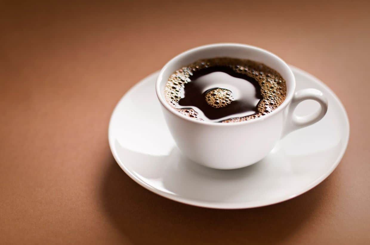 A cup of coffee on a saucer on a brown background.