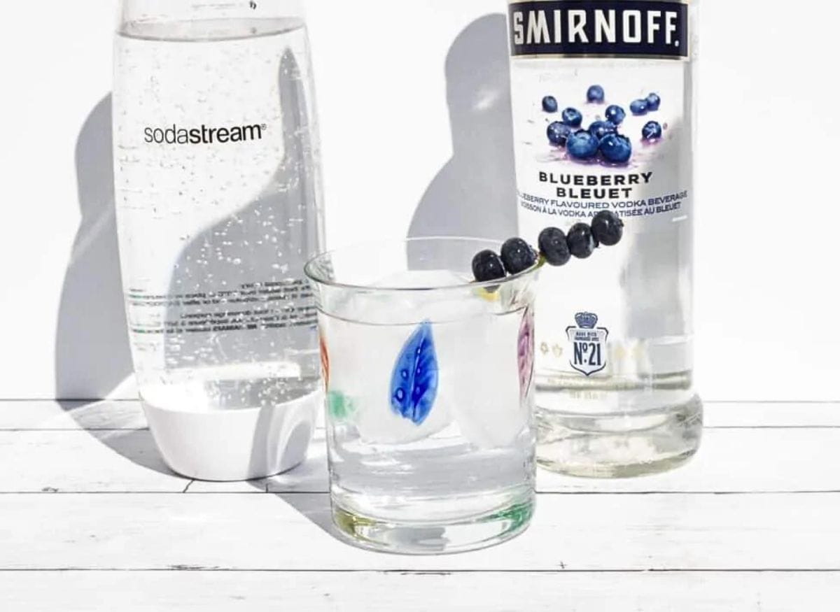 A bottle of vodka next to a glass with blueberries.