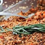 A dish of granola with cranberries and sprigs of rosemary.