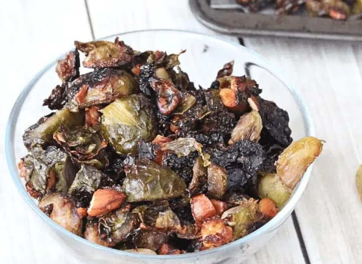 glass bowl with roasted brussels sprouts and more sprouts on a baking tray behind it.