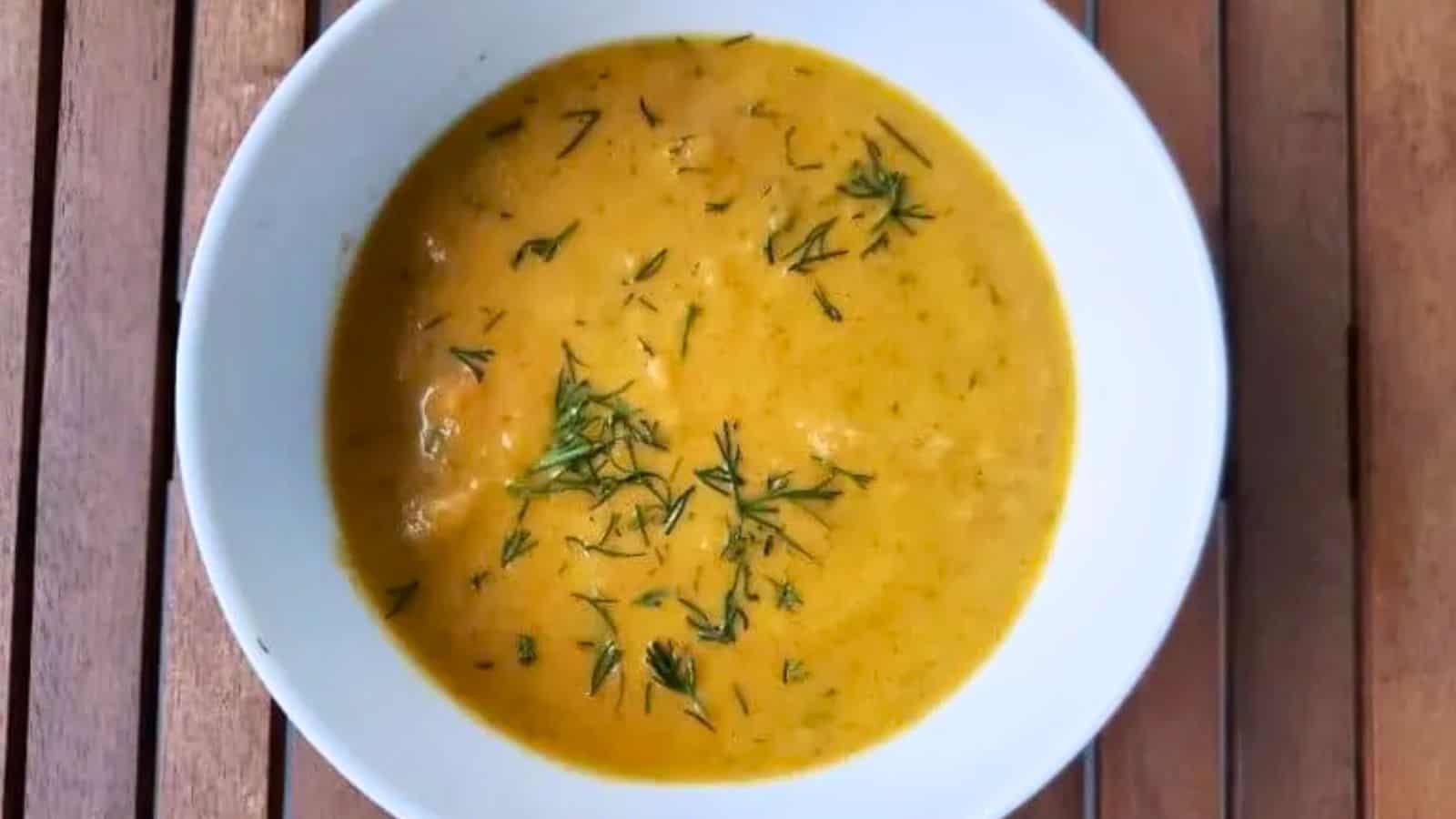 Image shows A bowl of carrot ginger soup sprigs of dill.