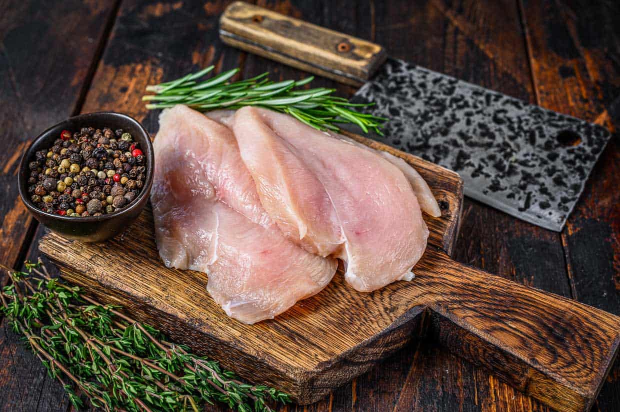 Fresh chicken cutlets on a wooden cutting board seasoned with herbs and spices.