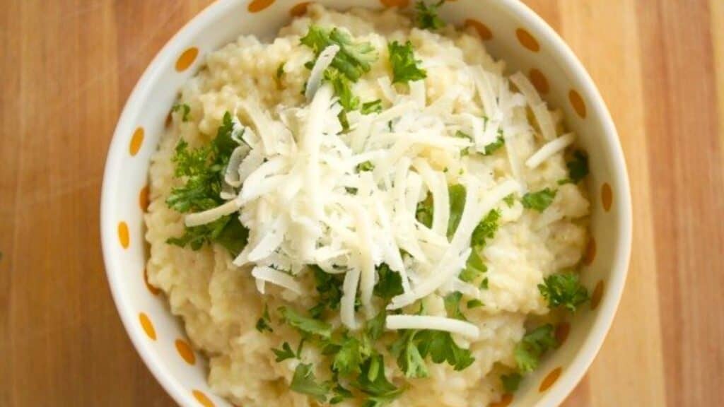 Image shows a bowl of chicken and pea risotto with parmesan cheese and parsley.