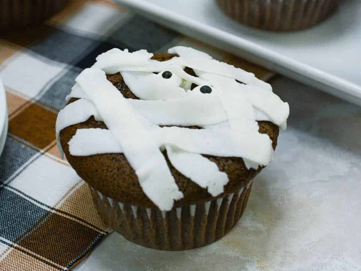 A chocolate mummy cupcake with white frosting on a table.
