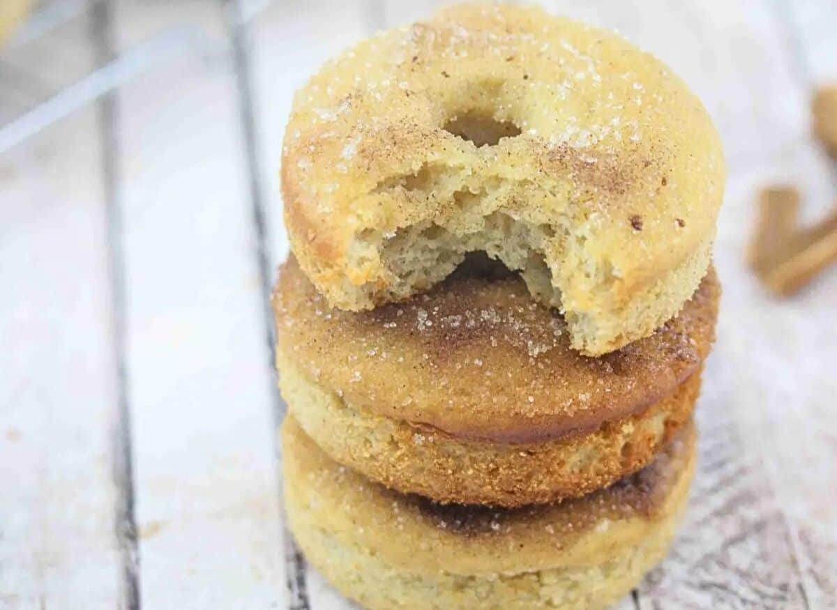 Cinnamon sugar protein donut with a bite out of it on a cooling rack with more donuts around ti and cinnamon beside it.
