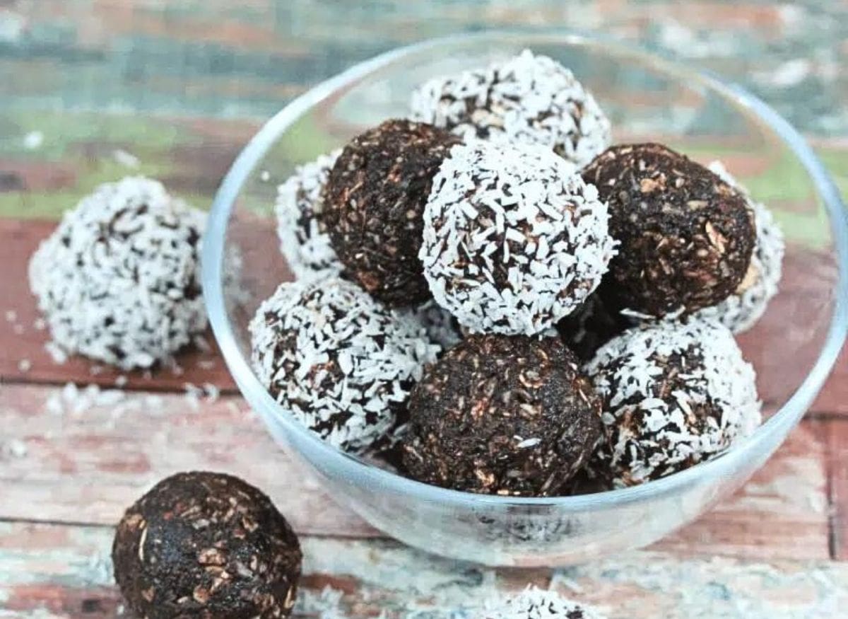 Chocolate coconut energy balls with dates in a glass bowl with three energy balls beside the bowl and coconut around it.