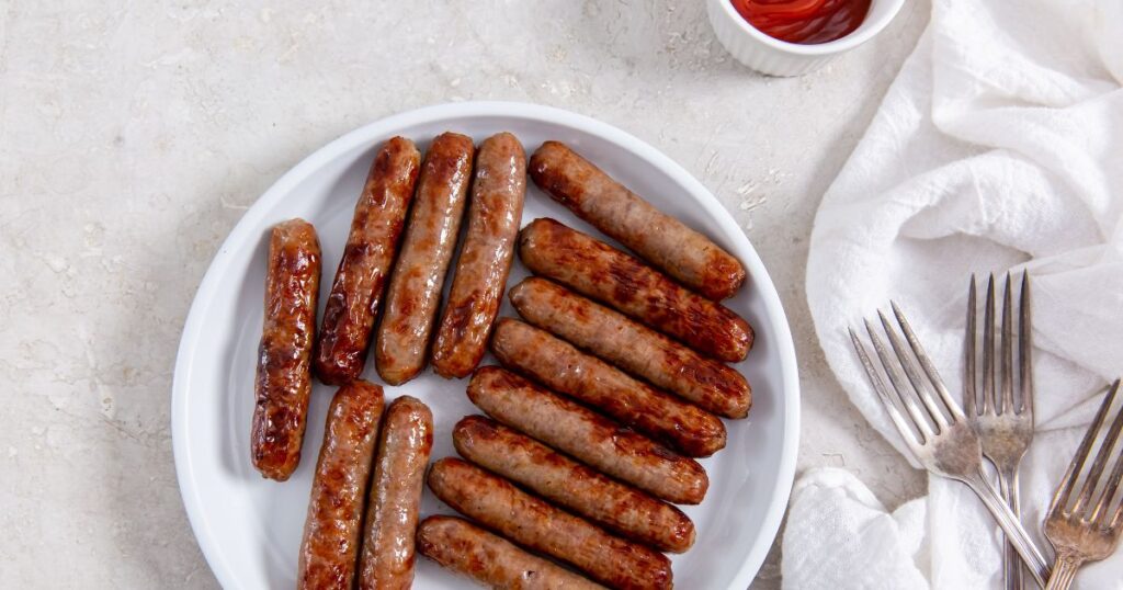 Sausages on a white plate with ketchup.