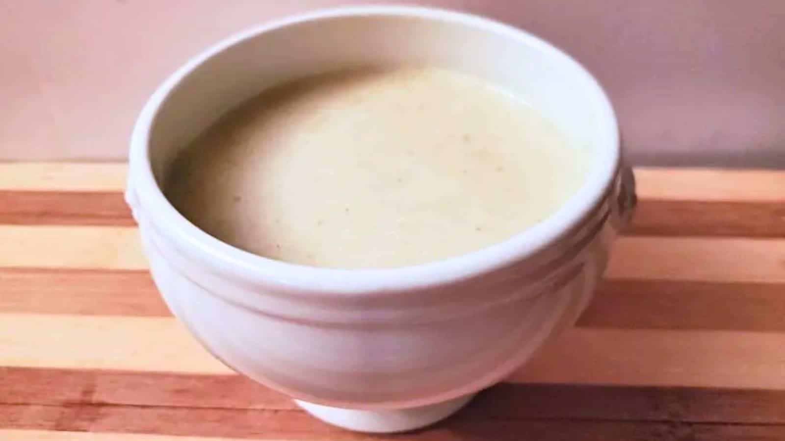 Image shows A white cup of cream of celery soup on a wooden cutting board.
