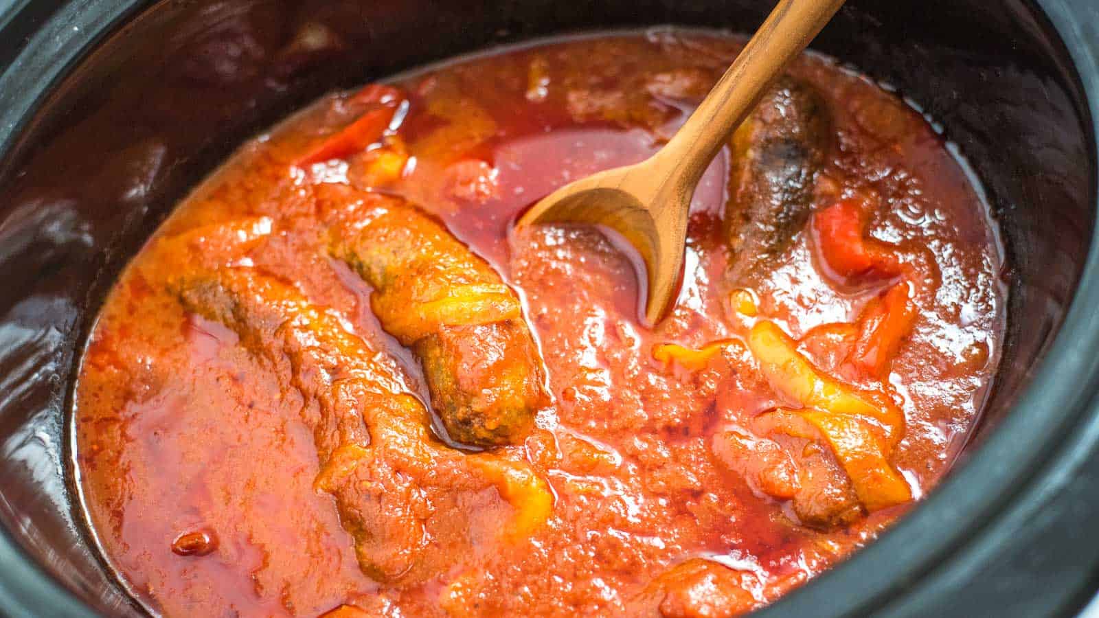 A crock pot full of sausage, peppers, and marinara sauce.