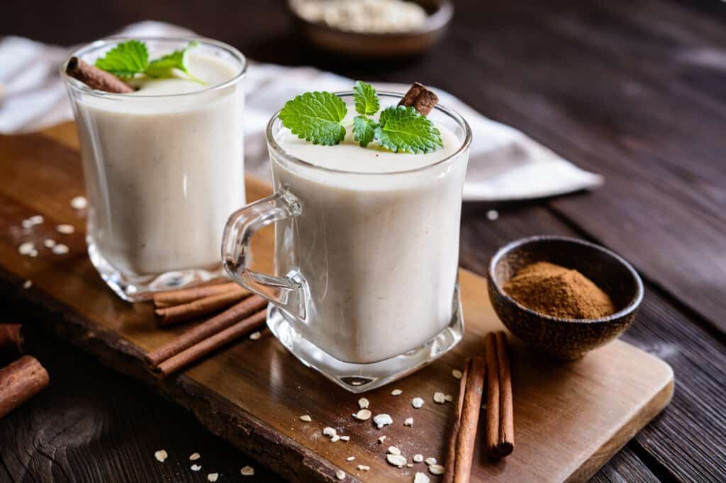 Two glasses of milk with cinnamon and cinnamon sticks on a wooden cutting board.