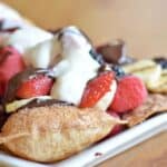 Image shows dessert nachos on a plate topped with fruit and whipped cream.