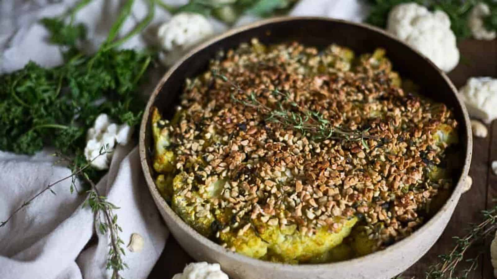 A bowl of cauliflower gratin topped with nuts and herbs.
