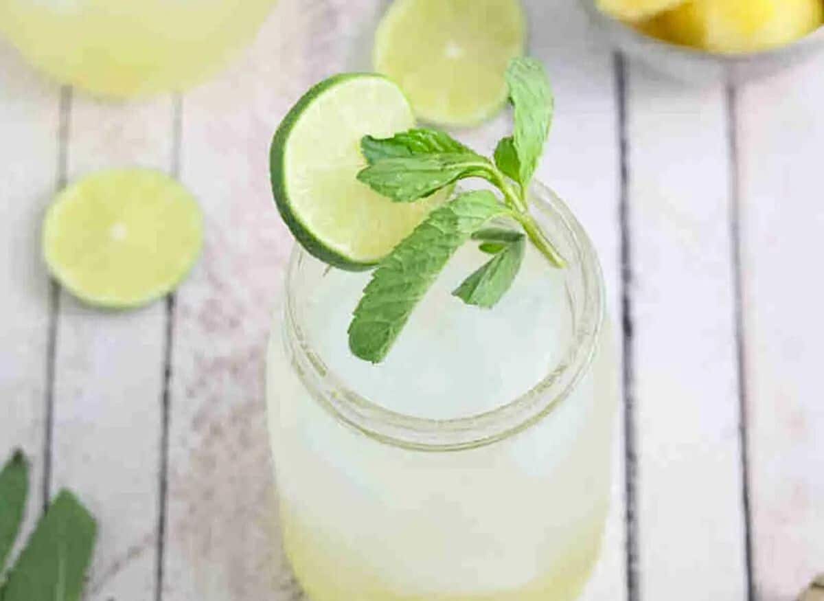 Ginger beer mocktail in a mason jar with fresh mint and lime on the jar and ingredients and another jar around it.