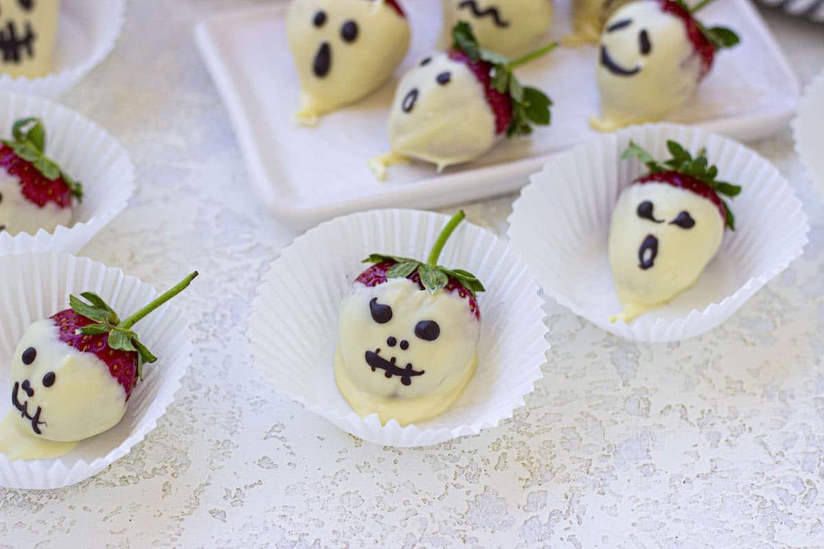 Several chocolate covered strawberries decorated as Halloween ghosts on the table.