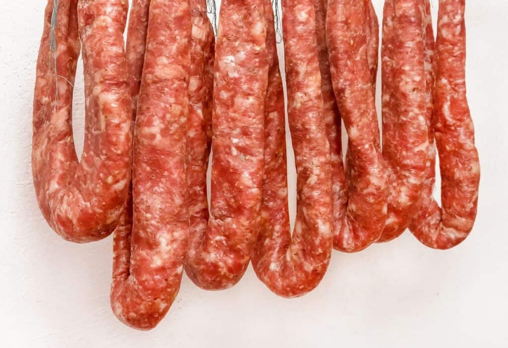 Image shows A group of sausages hanging on a white wall.