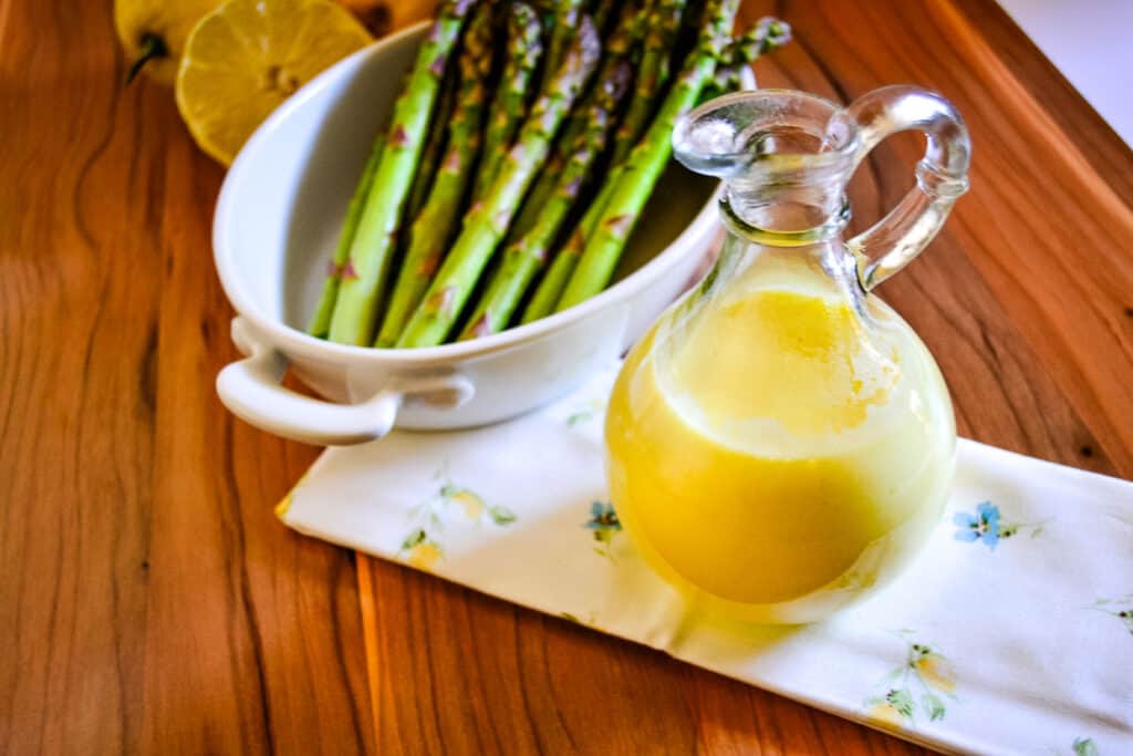 A jug of hollandaise sauce next to a bowl of asparagus.