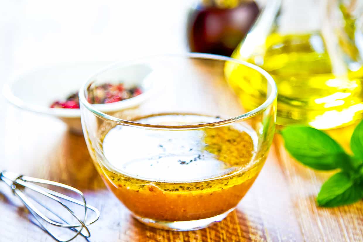 A glass of dressing with a whisk on a wooden table.