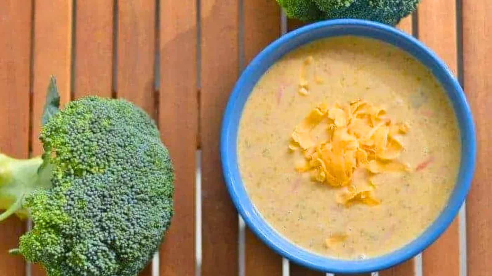Image shows A bowl of broccoli cheddar soup with broccoli around it.