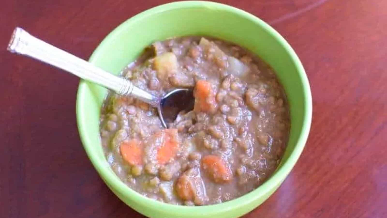 Image shows A bowl of lentil soup with a spoon in it.