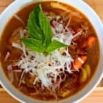 Image shows A bowl of italian meatball soup with a basil leaf on top.