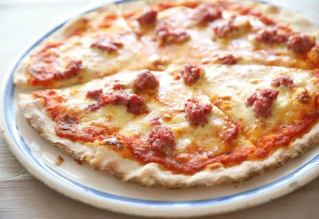 Image shows A pizza with Italian sausage and cheese on a plate.