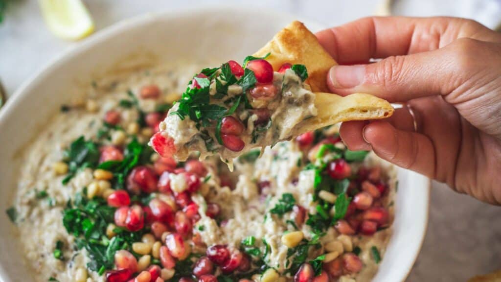 A hand is holding a bowl of sizzling pomegranate dip.