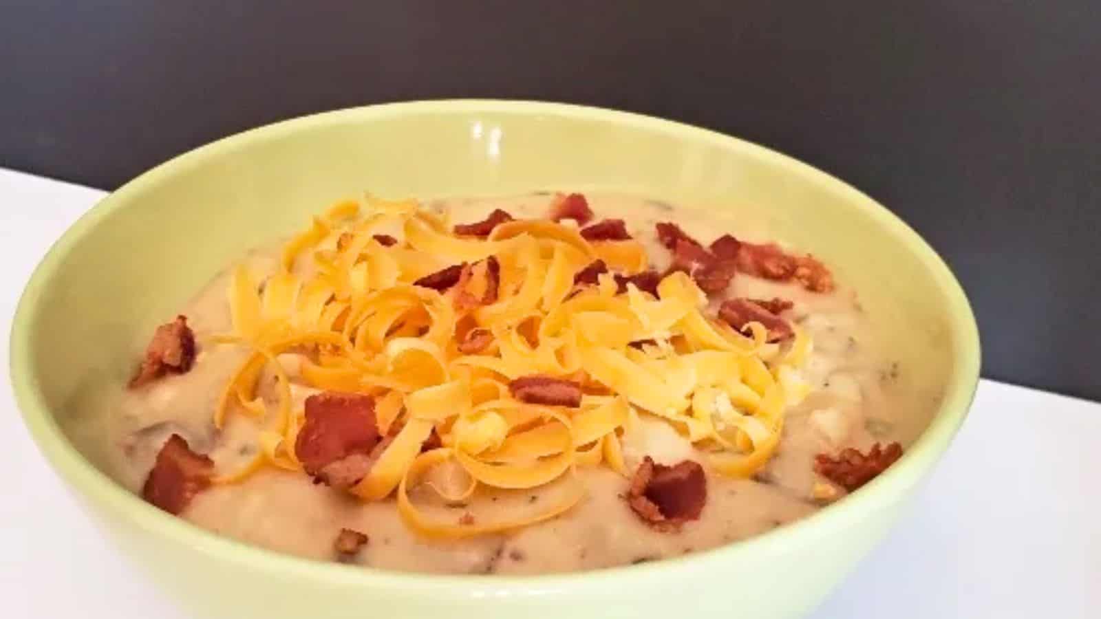 Image shows A bowl of cheesy loaded baked potato soup with bacon and cheese.