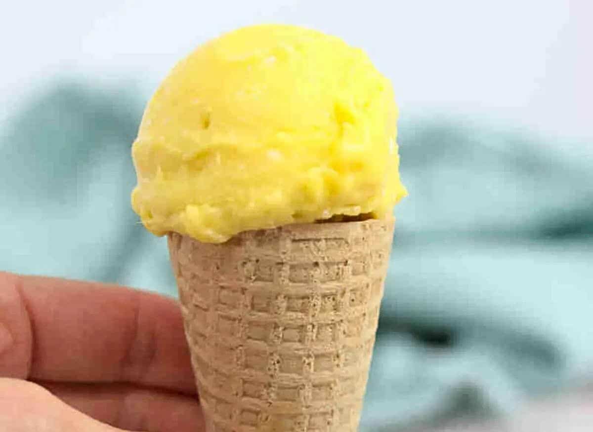 Close up of homemade mango ice cream in a gluten-free cone being held between fingers.