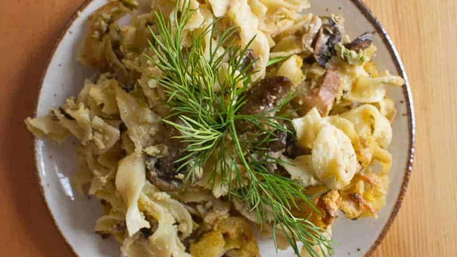 A plate of pasta with mushrooms and sprigs of dill.