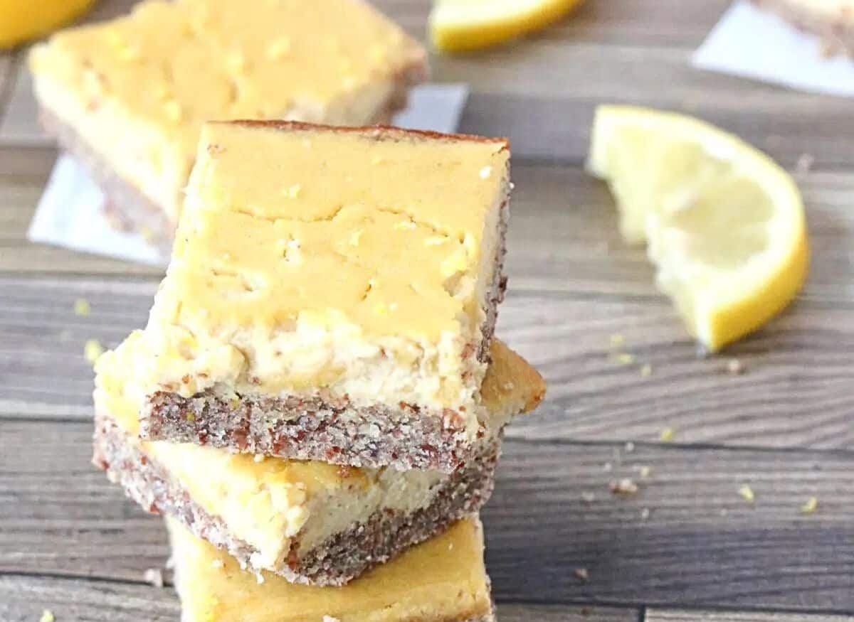 Three paleo lemon bars stacked with cut lemons around it and more behind them.