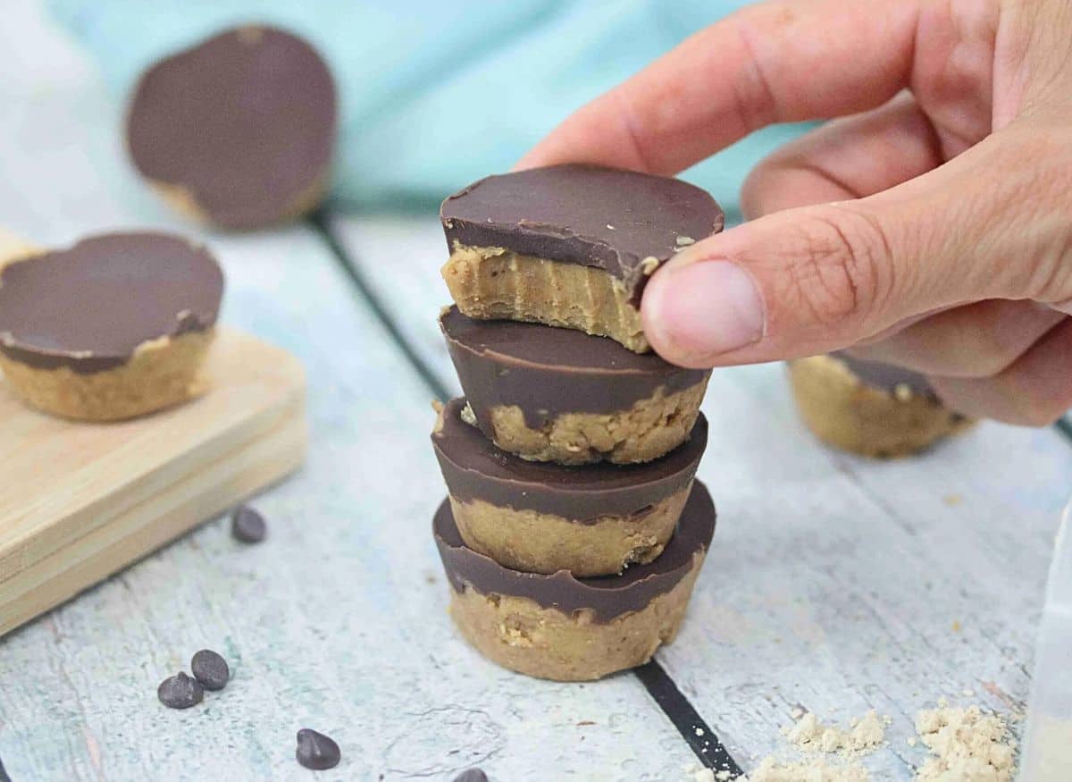 Four chocolate peanut butter cups stacked together with fingers placing the last one with a bite out of it on top.