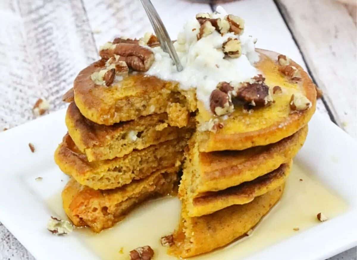 A stack of pumpkin pancakes with whipped cream and pecans.