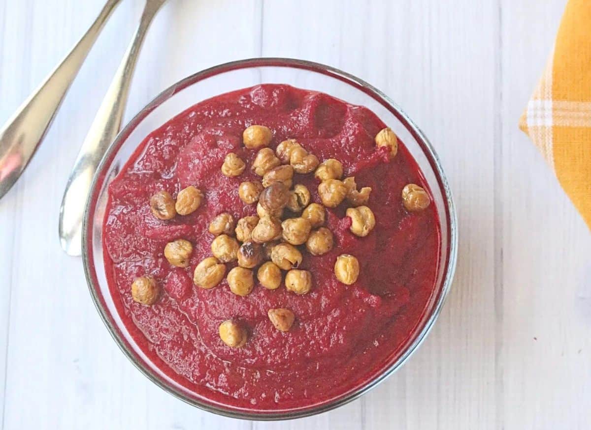 two glass bowls filled with healthy beet soup and topped with chickpeas. Two spoons beside the first bowl and a yellow napkin.
