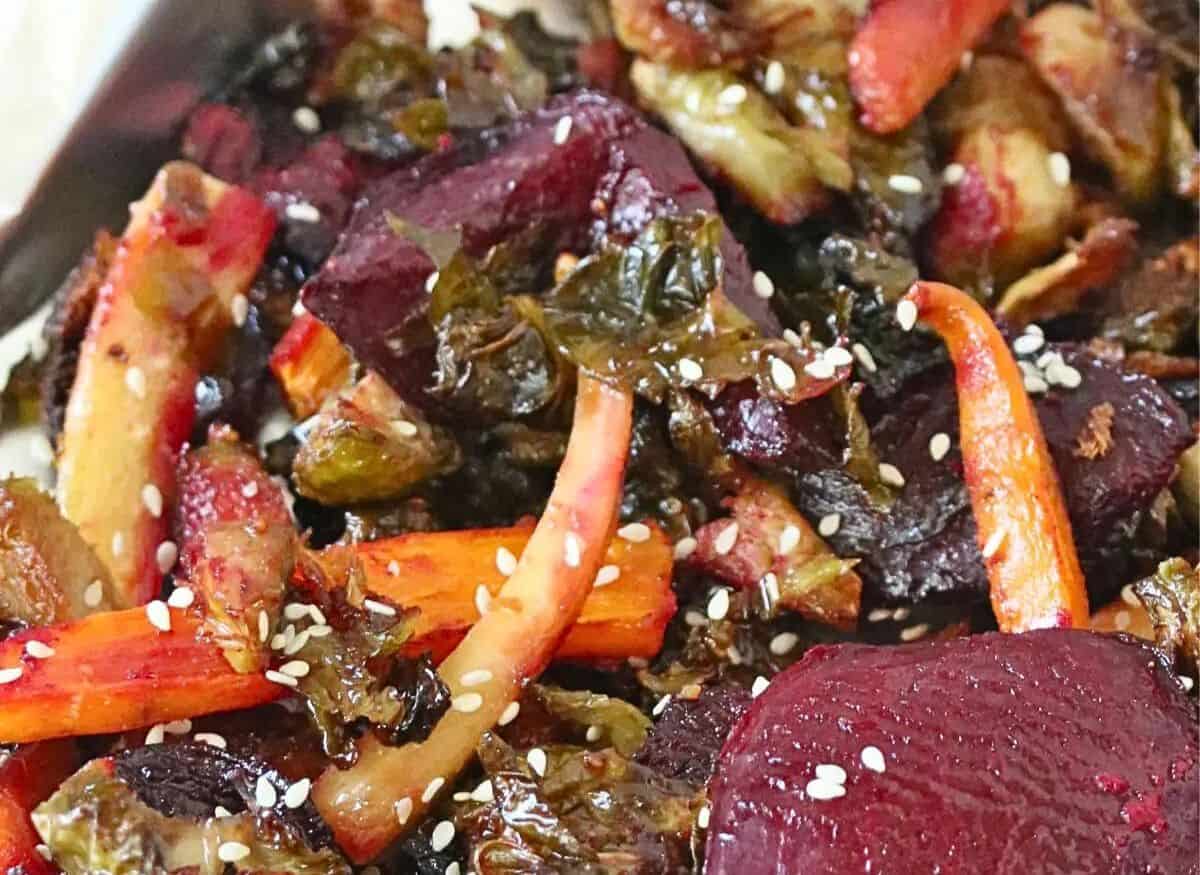Roasted carrots, beets and Brussels sprouts on a tinfoil lined pan topped with sesame seeds.