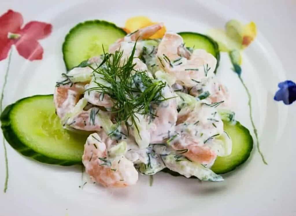 A plate with shrimp salad and cucumbers on it.