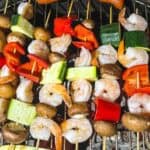 Skewers of vegetables and shrimp on a grill.