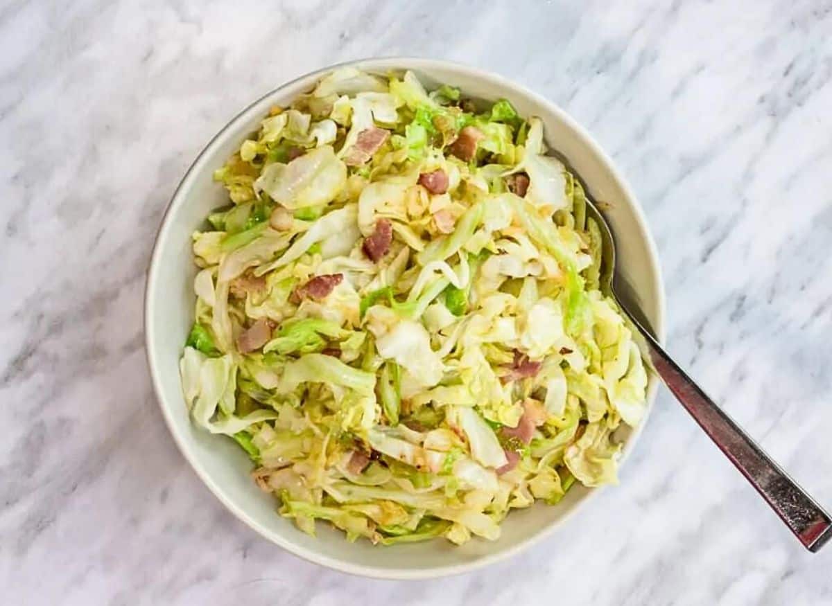 A bowl of cabbage salad with ham and bacon.