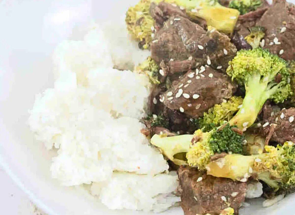 White bowl with beef and broccoli and rice with someone holding chopsticks over it.