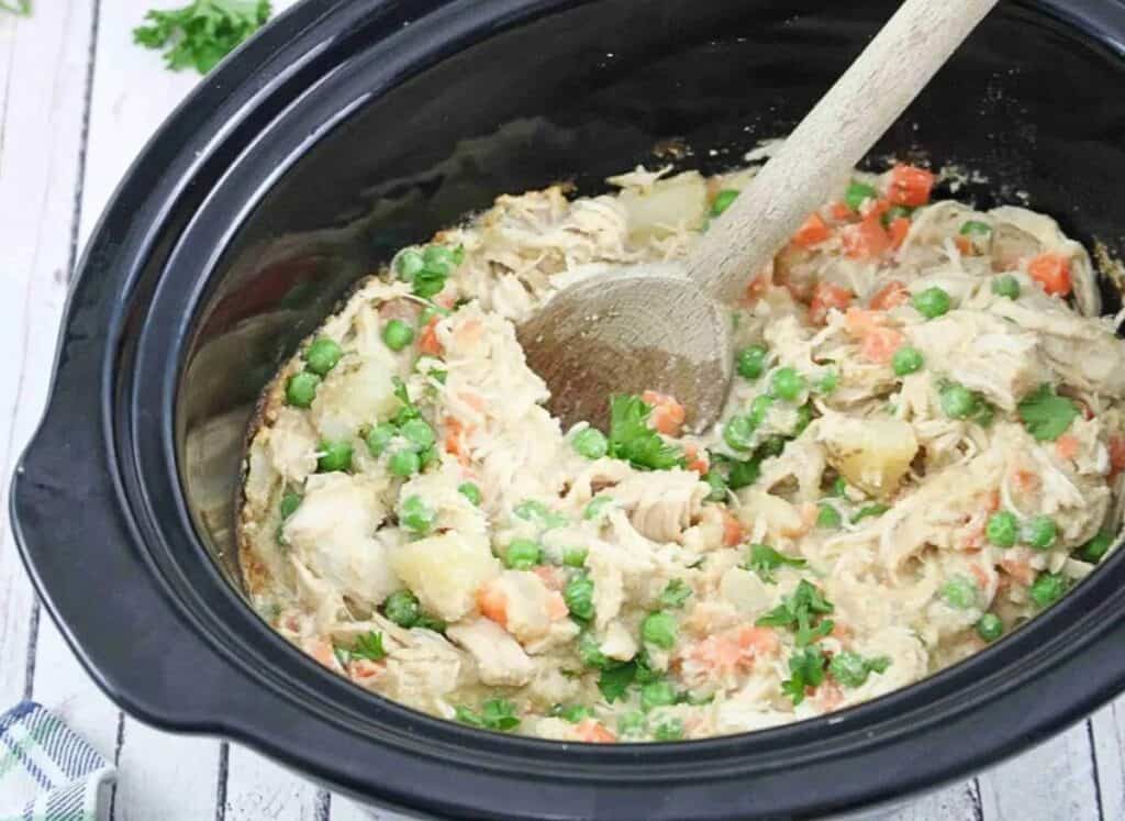 Chicken and peas in a crock pot with a wooden spoon.