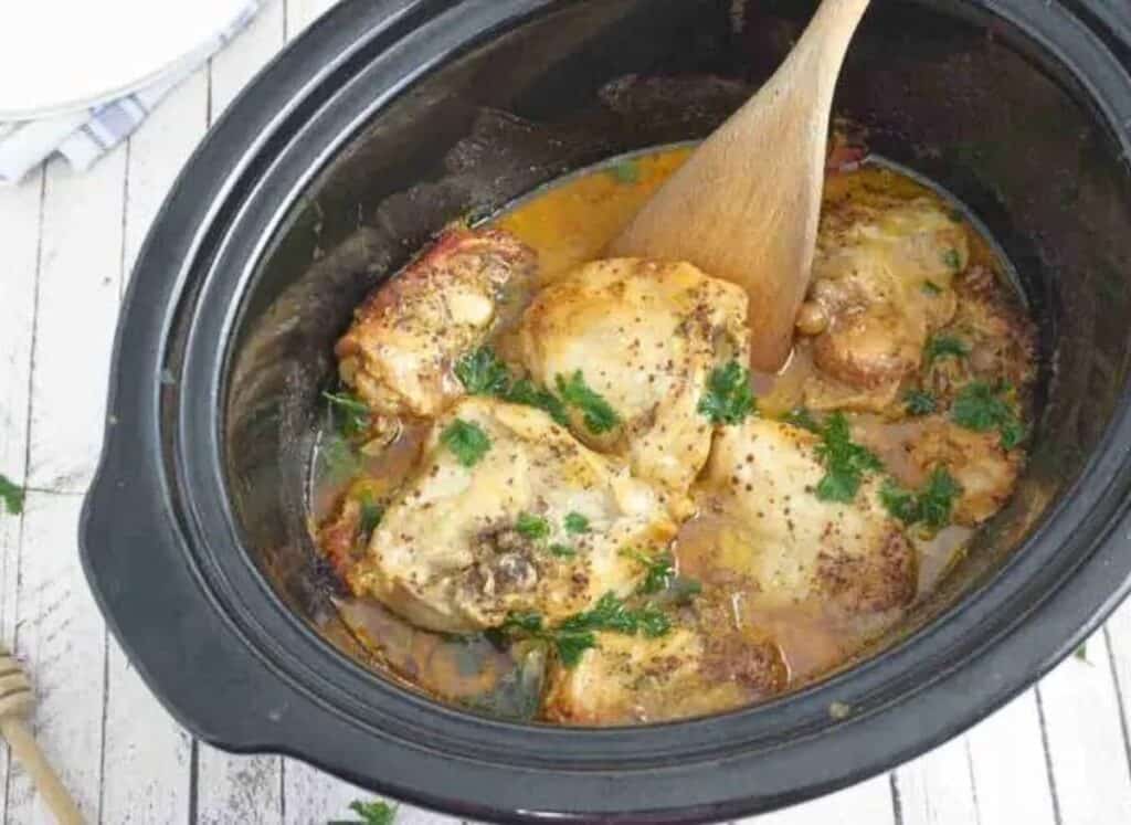 Chicken in a slow cooker with a wooden spoon.