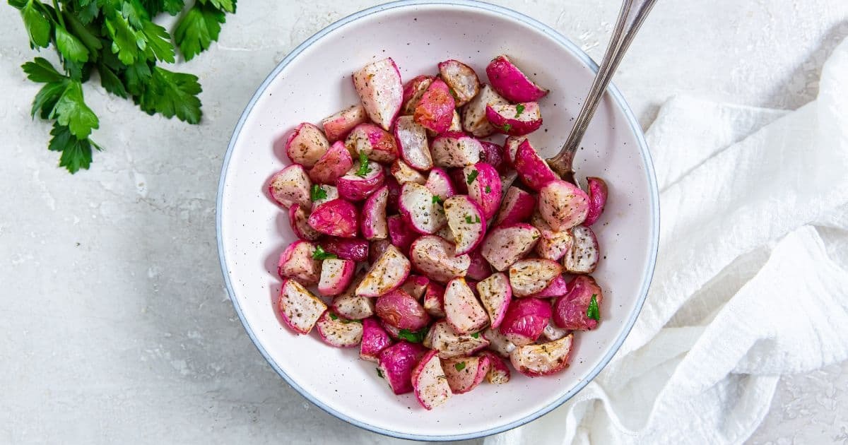Air Fryer Radishes with parsley, salt, and pepper in a white bowl with a spoon.